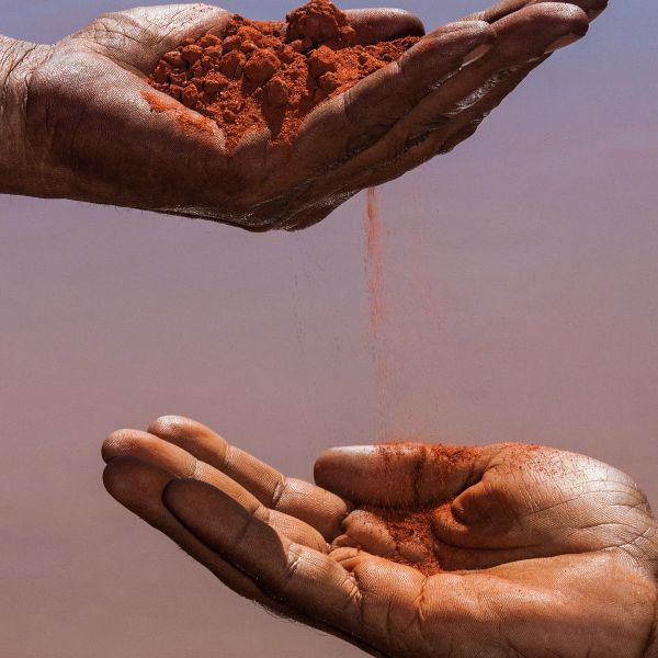 Hands passing red soil between each other.
