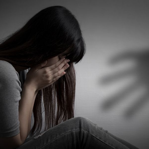 A woman sits on the floor, covering her face in distress.