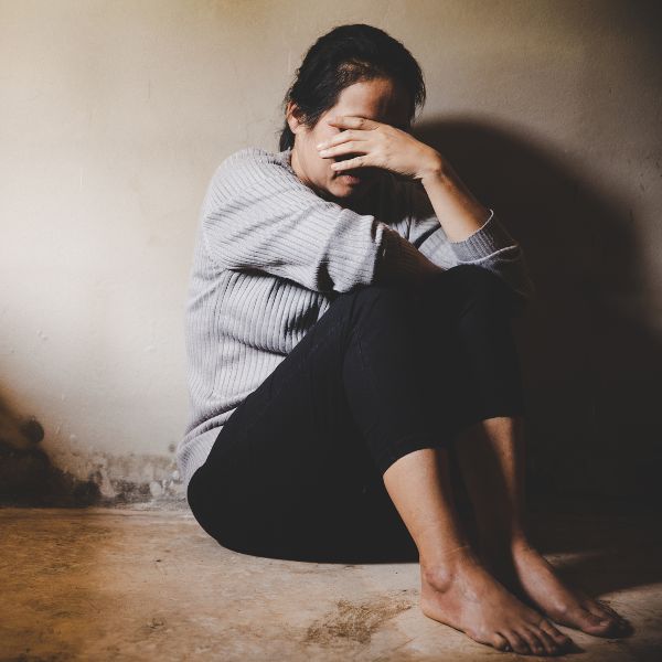 A woman sits on the floor with her hands covering her face, symbolizing trauma or anxiety.