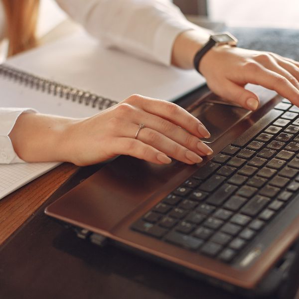 Woman typing on a laptop with a notepad, signifying focus and productivity during healing consultation booking